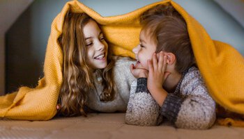 Ein Junge und ein Mädchen haben eine Decke auf ihrem Kopf und lachen sich an | © BraunS - Getty Images/iStockphoto